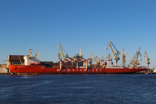 Red cargo ship docked at St. Petersburg harbor with cranes under a clear blue sky.