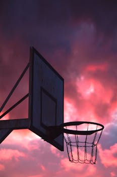 Silhouette of a basketball hoop set against a dramatic pink and purple sky, perfect for mobile wallpapers.