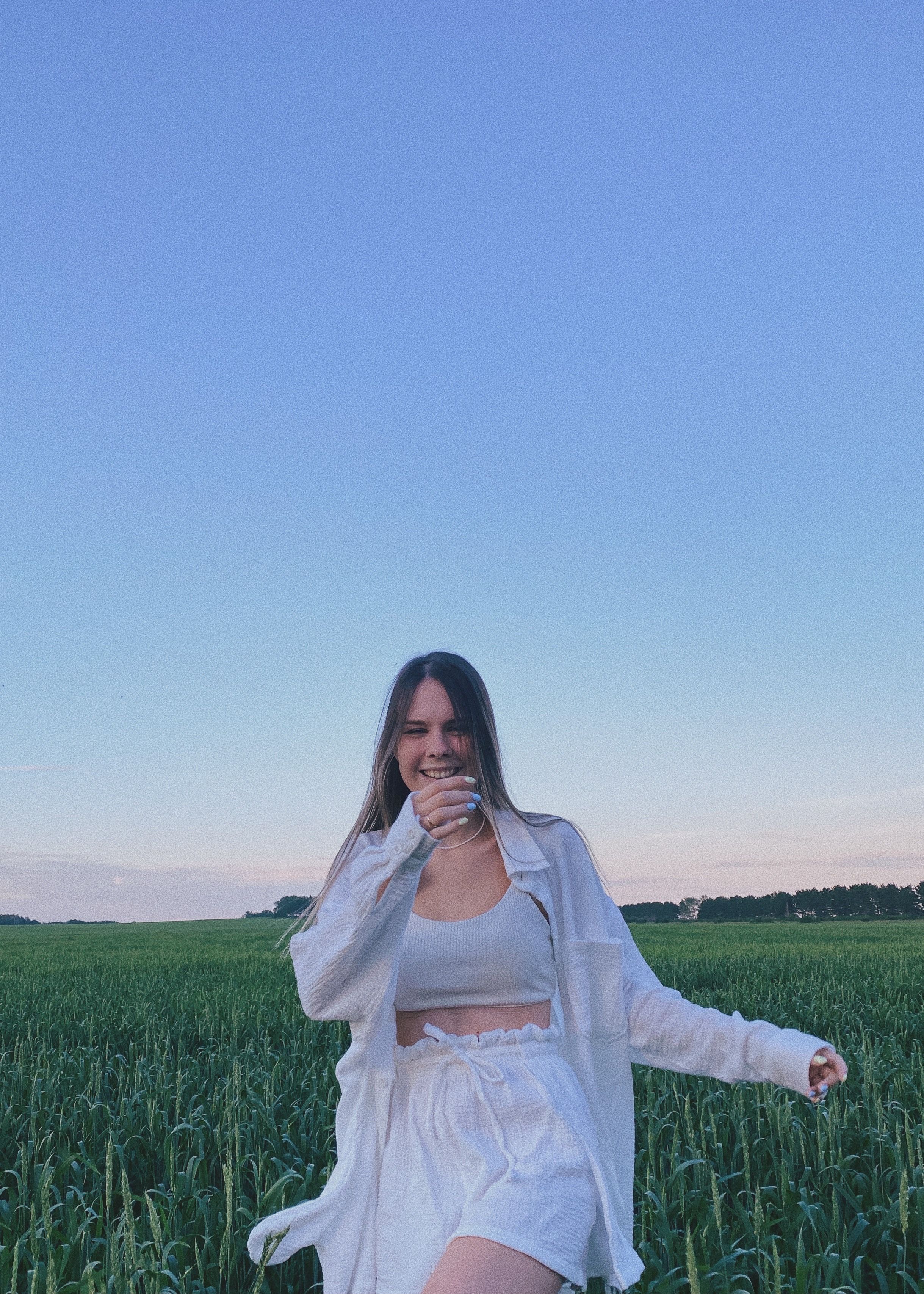 Caucasian woman joyfully smiling in a green field under a clear blue sky.