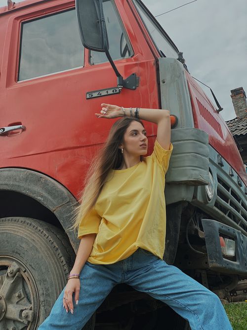 Free Young woman in yellow shirt poses confidently by a large red industrial truck outdoors. Stock Photo