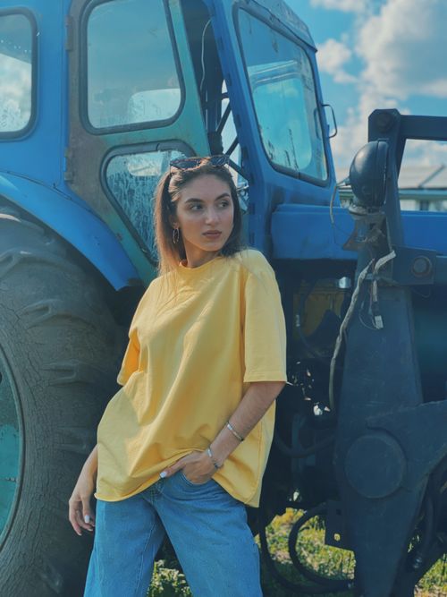 Free Casual portrait of a woman posing in a yellow shirt beside a blue tractor on a sunny day. Stock Photo