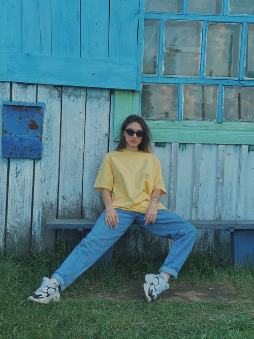 Free Young woman in casual attire posing on bench against rustic wooden backdrop. Fashion and style concept. Stock Photo