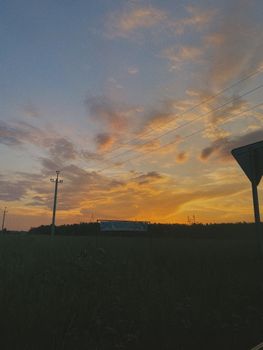 A serene sunset over a field with silhouetted power lines and clouds.