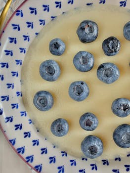 Close-up of fresh blueberries on a creamy dessert with a decorative plate.