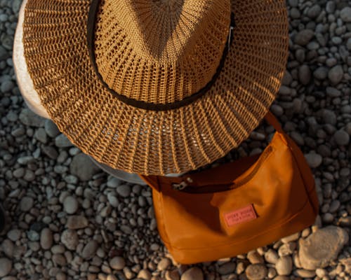 A Brown Woven Hat and A Shoulder Bag on Pebbles