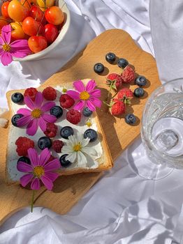 Colorful summer picnic setup featuring fresh berries, cosmos flowers, and a wooden board.