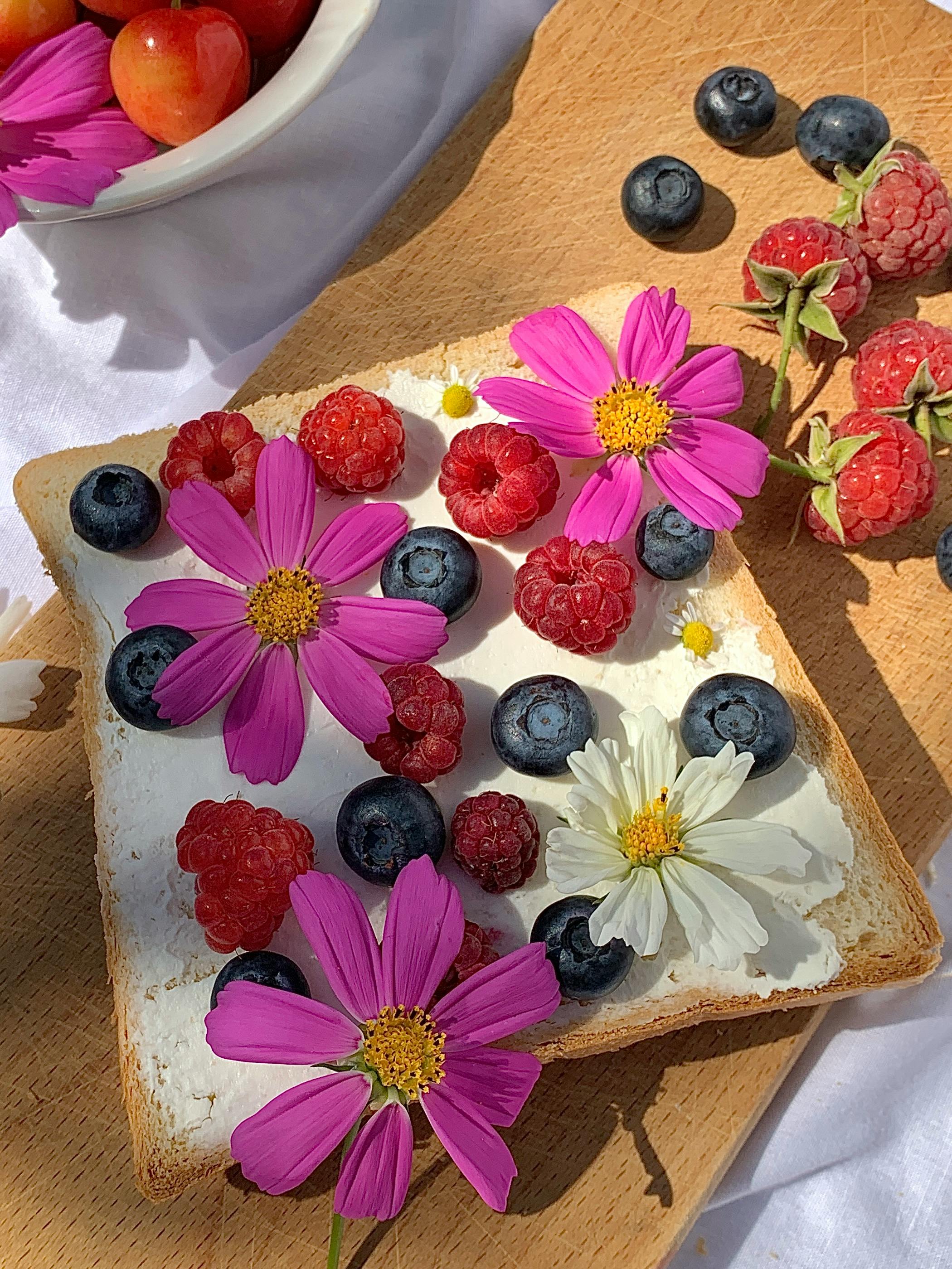Toast with raspberries, blueberries, and flowers on wooden board in natural light.