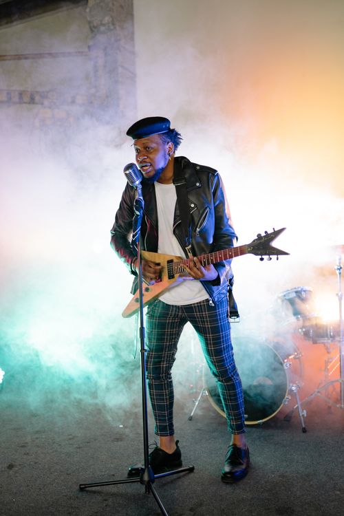 Free A dynamic musician playing guitar and singing on stage amidst vibrant smoke. Stock Photo