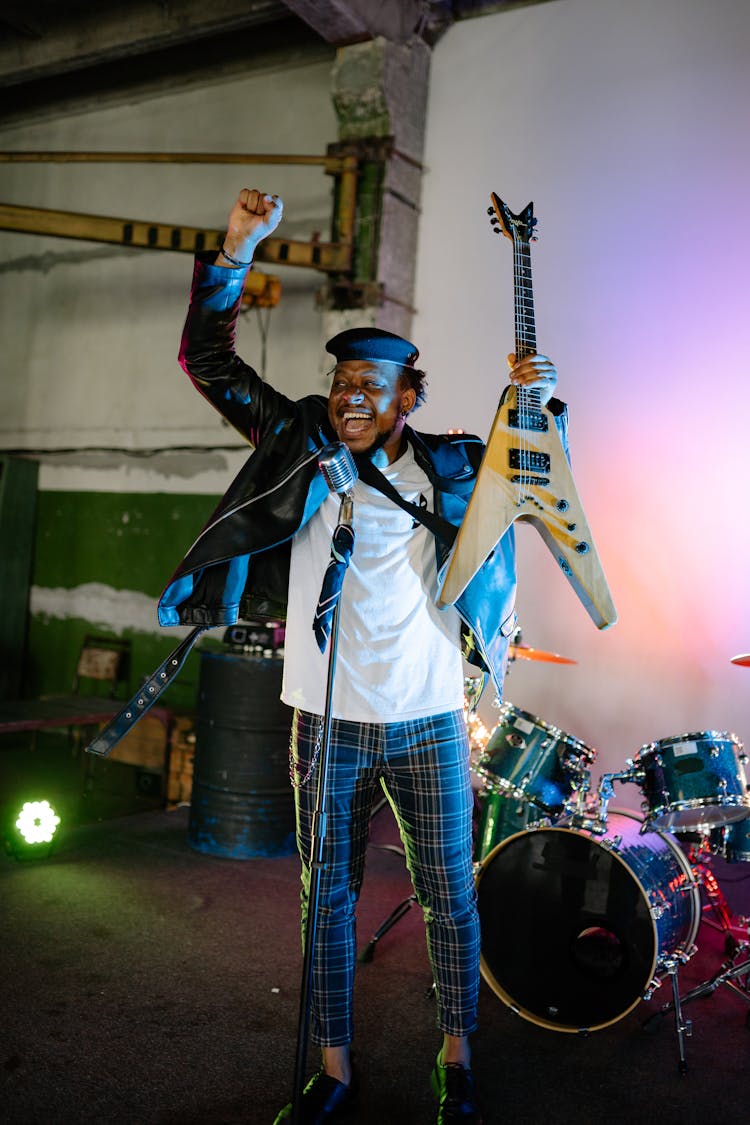 A Man Holding A Guitar And Standing In Front Of A Microphone Stand