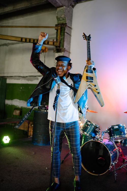 Free Dynamic indoor performance of a joyful musician holding a guitar and microphone. Stock Photo