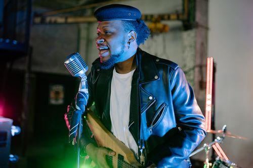Free Musician passionately singing with a guitar, wearing a black leather jacket and beret. Stock Photo