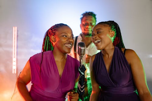 Women in Purple Top Smiling while Singing Together