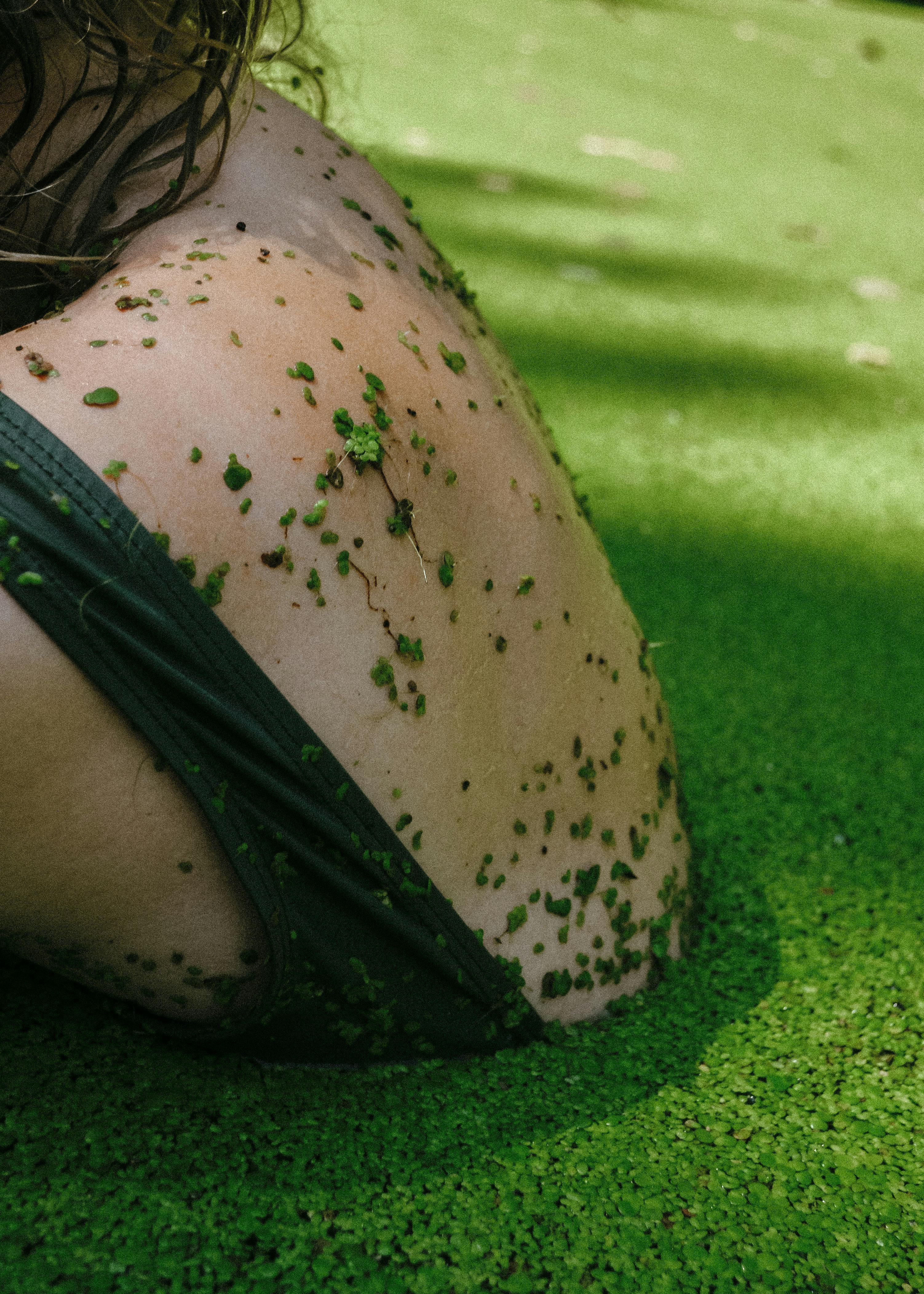 Close-up of person in tank top covered with green duckweed.