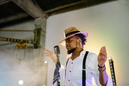 A passionate musician sings on stage with a vintage microphone and stylish hat.