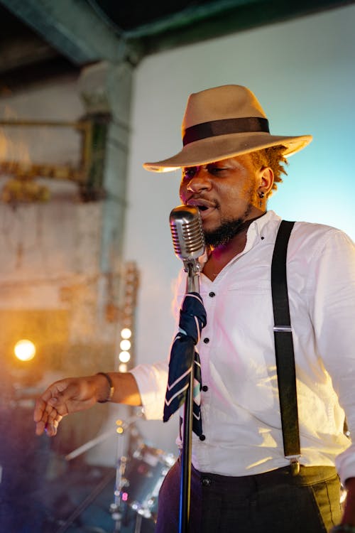 Free A Man Wearing a White Long Sleeve Shirt and a Brown Hat Singing Stock Photo