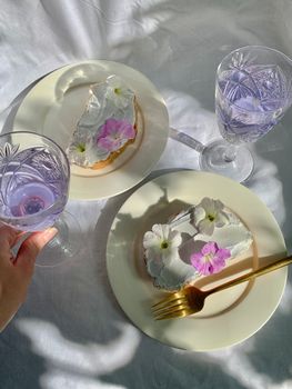Beautiful cakes with flowers and crystal glasses on a sunny white table.