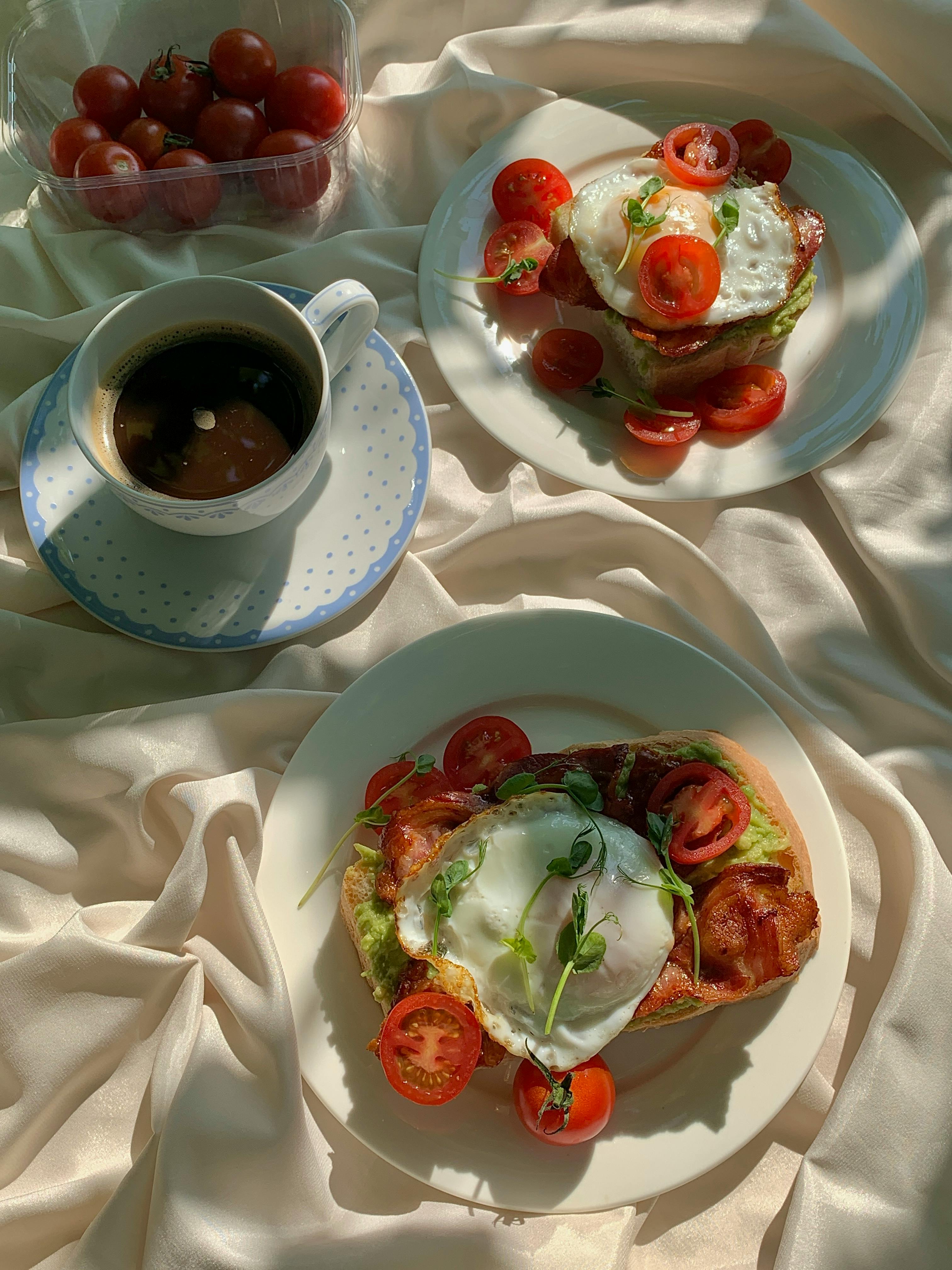 Delightful breakfast setup with bacon and egg avocado toast, cherry tomatoes, and coffee.