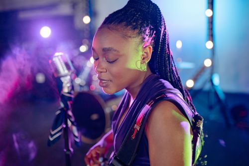 Free A talented female singer with microphone in a vibrant, colorful stage setting, showcasing her performance skills. Stock Photo