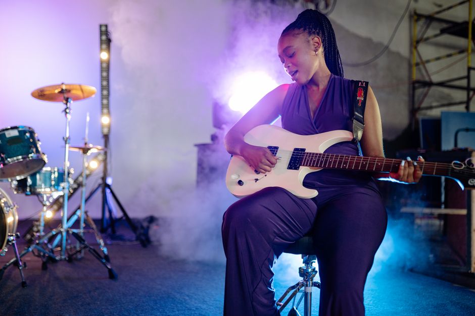 A woman passionately playing guitar on stage with vibrant lighting effects, creating an energetic atmosphere.