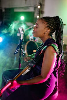 A female musician passionately singing and playing guitar under colorful stage lights.