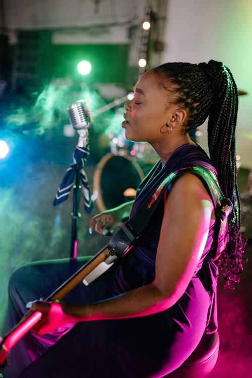 Free A female musician passionately singing and playing guitar under colorful stage lights. Stock Photo