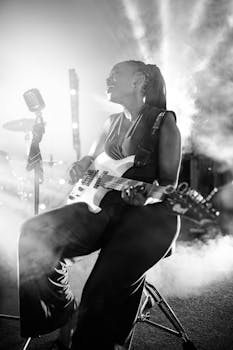 A captivating black and white image of a woman playing guitar in a smoky concert setting.