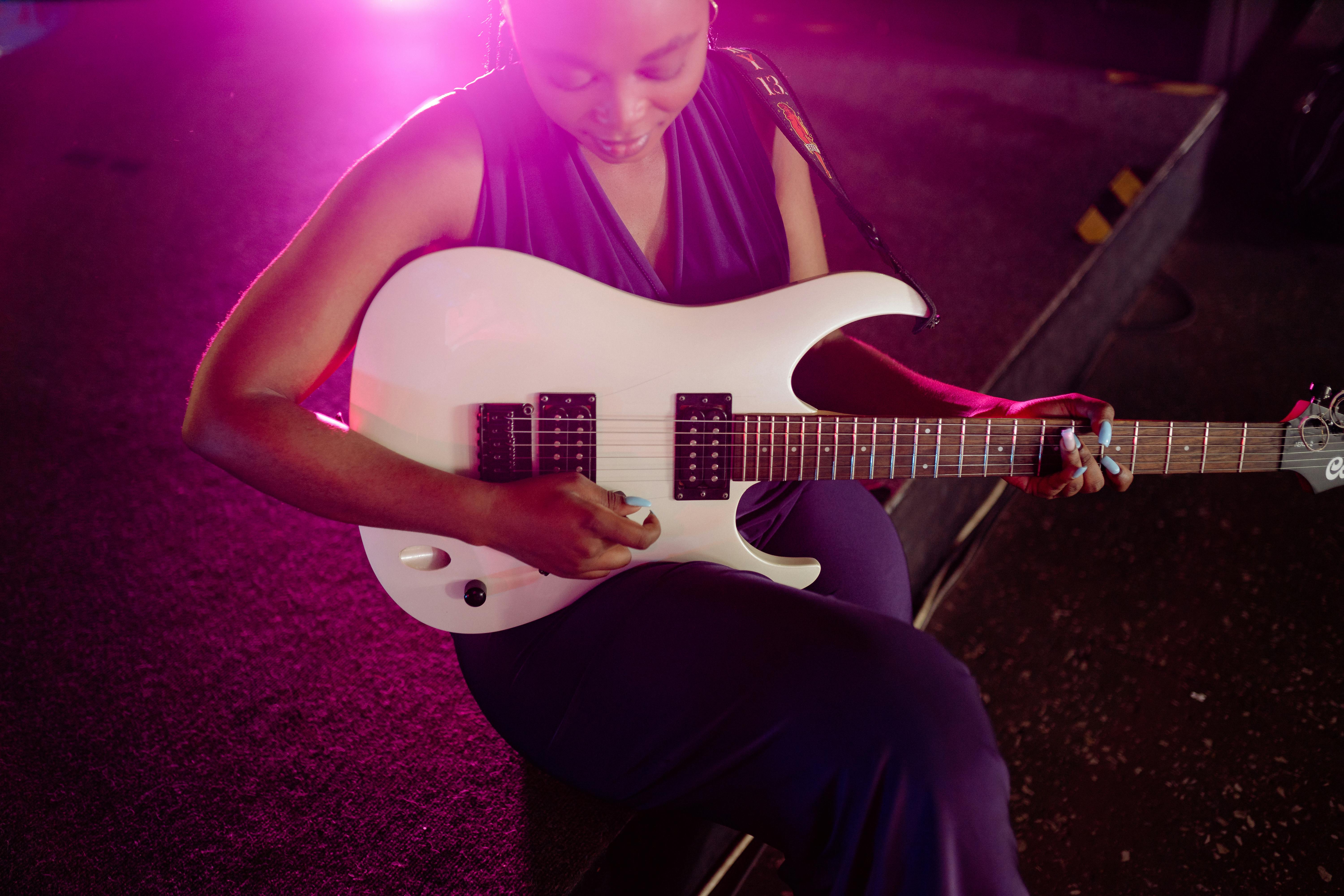 Woman performs on stage with a white electric guitar under vibrant pink lighting.