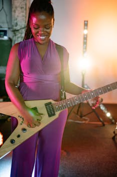 A woman in a purple outfit playing an electric guitar with stage lights in the background.