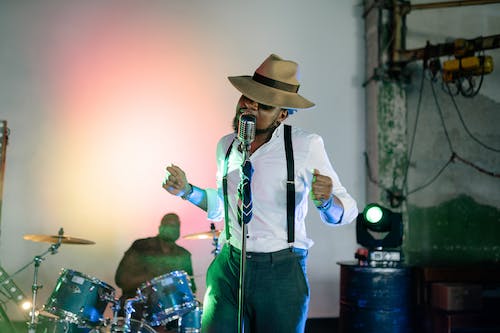 Man in White Shirt and Hat Standing and Singing