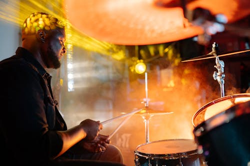 Man in Black Shirt Playing Drums Beside Yellow Light