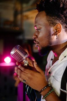 Side view of a male singer passionately performing with a vintage microphone on stage.