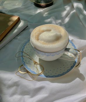 Elegant cup of cappuccino with generous foam on a saucer, set on a sunlit table.