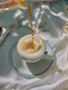 A Person Pouring a Brown Liquid on a Frothy Drink