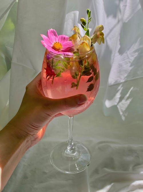 A Hand Holding Cocktail Drinks with Flower Petals Design