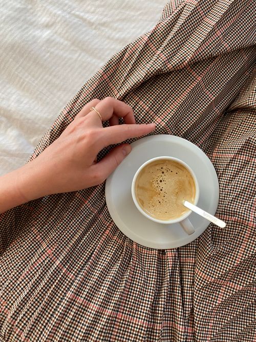 Free A cozy morning scene with a hand holding a cup of hot coffee on a patterned blanket. Stock Photo