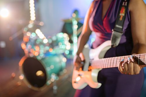 Free Close-up of a female guitarist playing on stage with drum set in background. Stock Photo