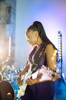 Woman playing electric guitar on stage, illuminated by vibrant lights during a live concert.