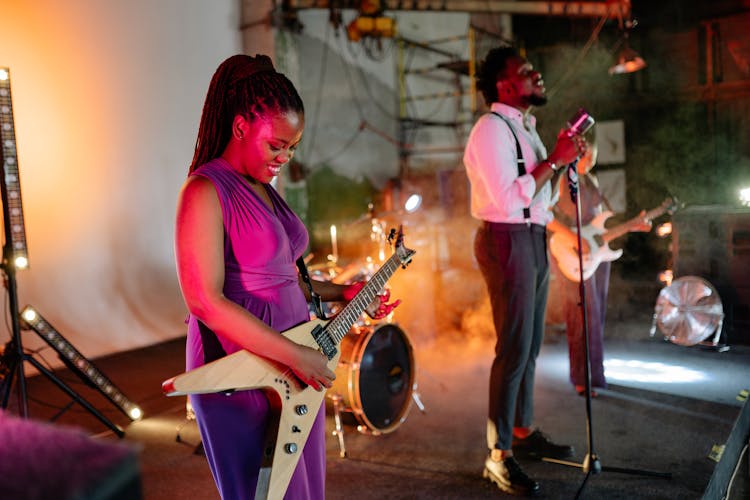 A Woman Playing The Bass Guitar Beside A Man Singing