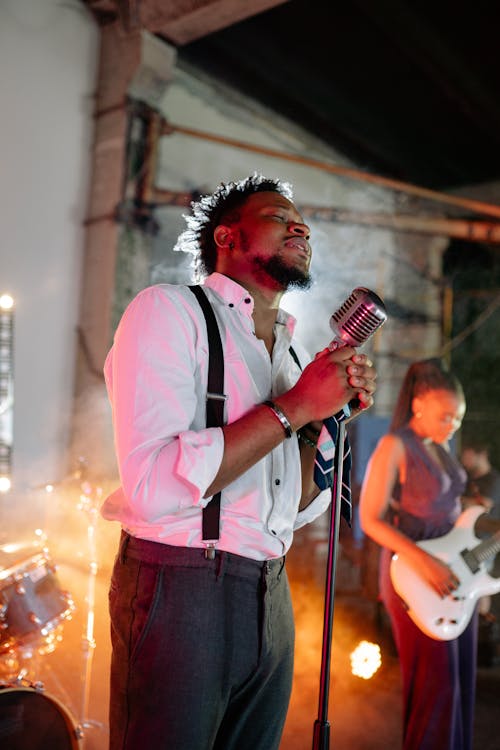 A Man in White Long Sleeve Shirt Holding Microphone While Singing