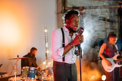 Free A vibrant indoor band performance featuring a singer, drummer, and guitarist in action. Stock Photo