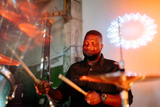 A joyful Black male drummer playing indoors with dynamic lighting and vibrant backdrop.