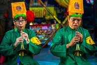 A Pair of Men in Green Long Sleeve Uniforms with Yellow Hats Playing the Trumpets