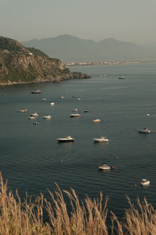 Free A serene view of boats floating near coastal cliffs with mountain backdrop, perfect for travel inspiration. Stock Photo