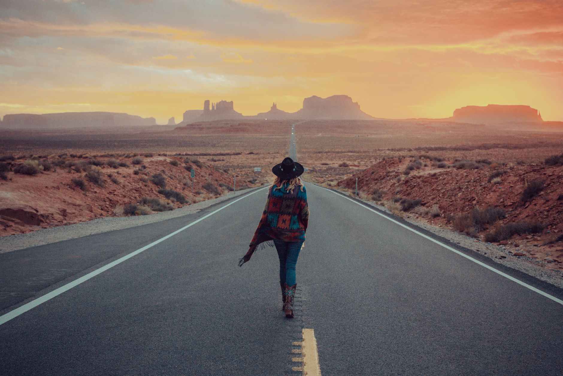 Woman walking on a scenic road in Monument Valley, Arizona during sunset.