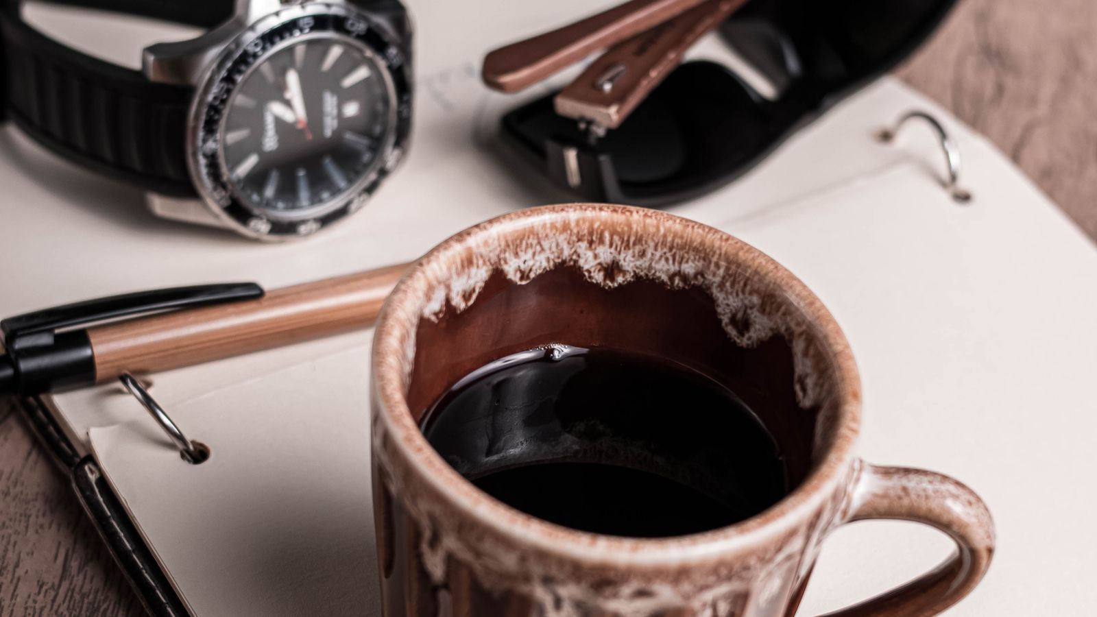 Coffee mug beside a notebook, pen and wristwatch