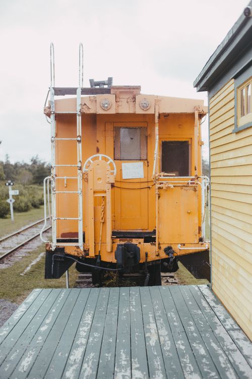 Free A vintage yellow caboose sits on train tracks beside a wooden building. Stock Photo
