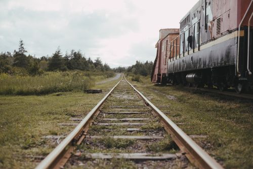 Free A tranquil scene of railroad tracks stretching into the horizon beside a rustic train in a verdant landscape. Stock Photo