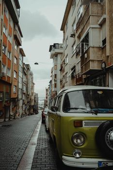 A classic green Volkswagen van parked on a cobblestone street surrounded by city buildings on a rainy day.