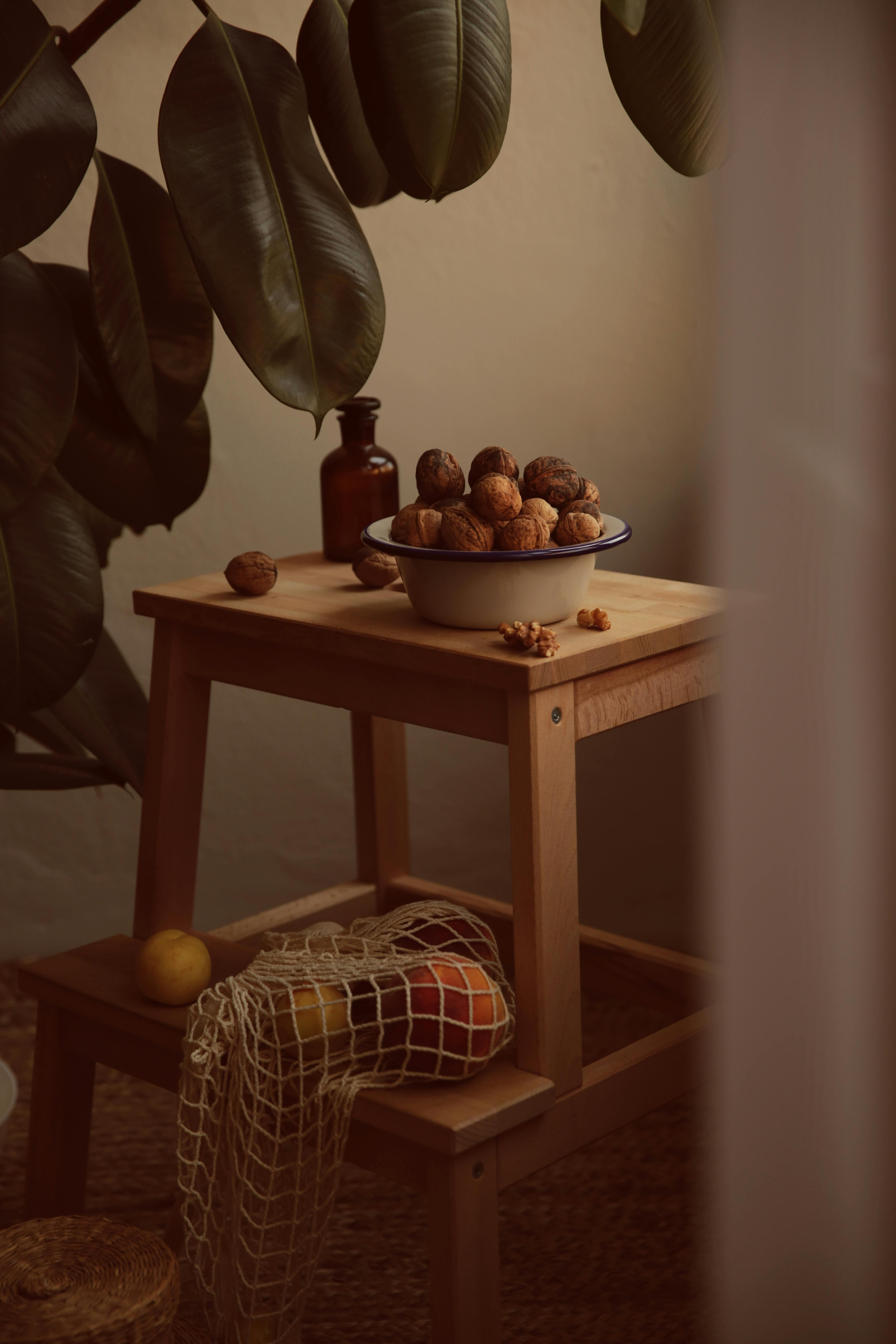 Warm rustic setup featuring walnuts, a mesh bag of fruit, and green leaves indoors.