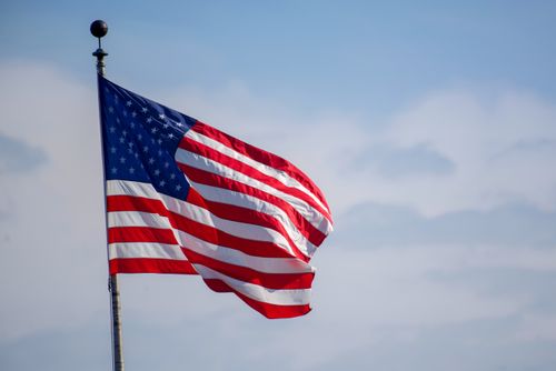 Free American flag waving on flagpole against a blue sky, symbolizing patriotism. Stock Photo